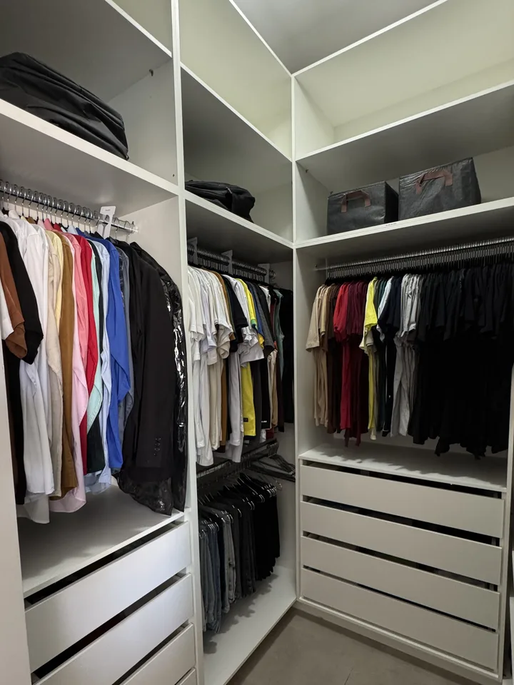 Closet masculino com camisas e camisetas agrupadas por cor em araras e gavetas embaixo