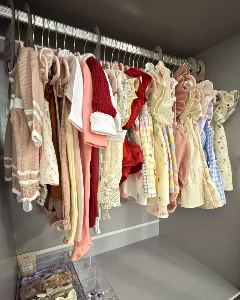 Guarda-roupa de bebê com roupinhas em cabides iguais e bandejas de faixas e sapatinhos embaixo