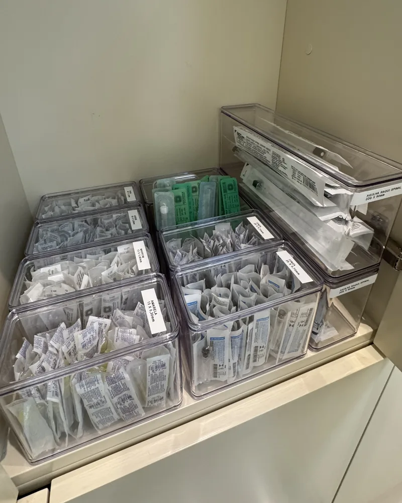 Armário de consultório com caixas transparentes etiquetadas por tipo e calibre de agulha